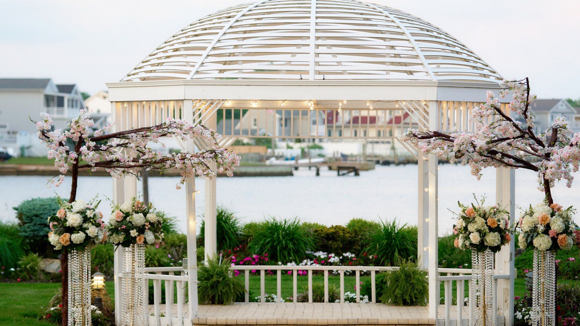 A white gazebo decorated with flowers and branches overlooking a body of water.