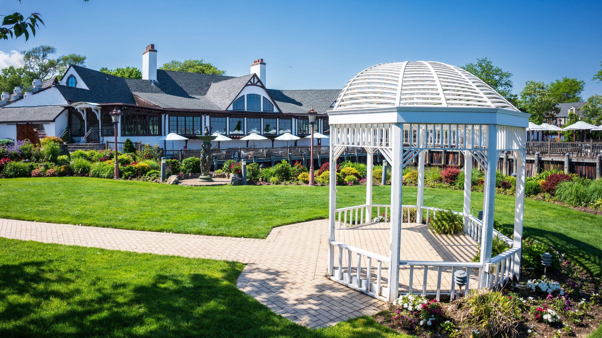A white gazebo is in the middle of a lush green field in front of a house.