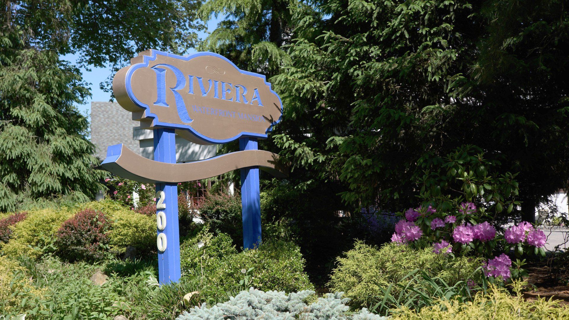A sign for riviera is surrounded by bushes and trees