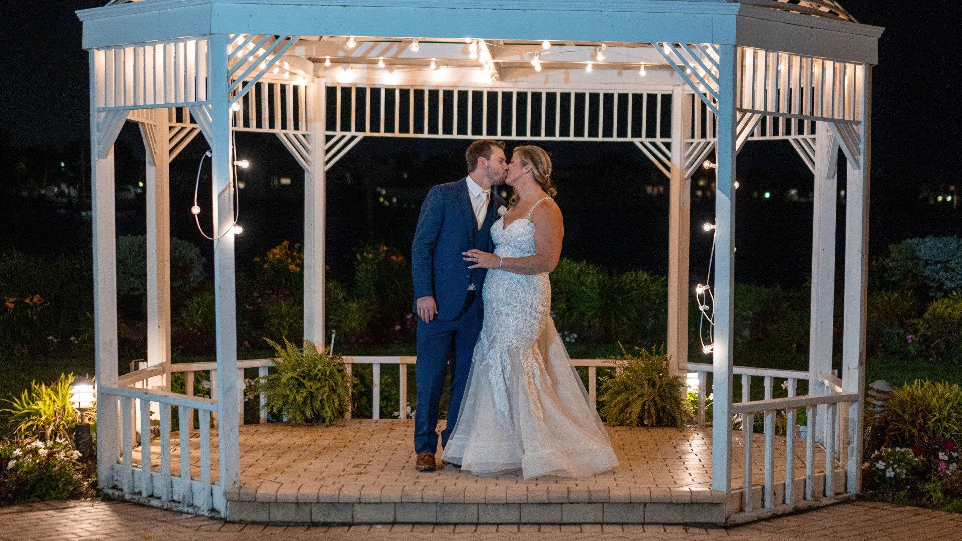 A bride and groom are kissing under a gazebo at night.
