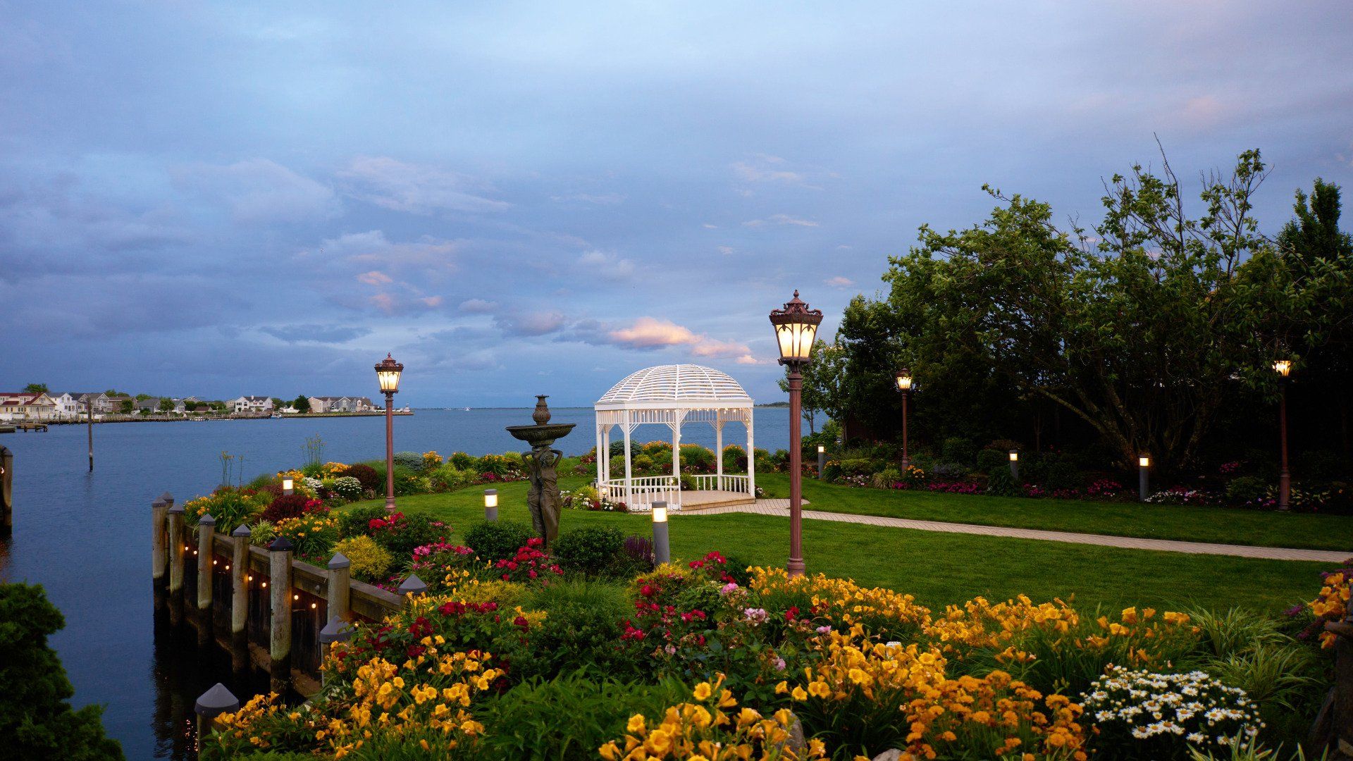 There is a gazebo in the middle of a garden next to a body of water.