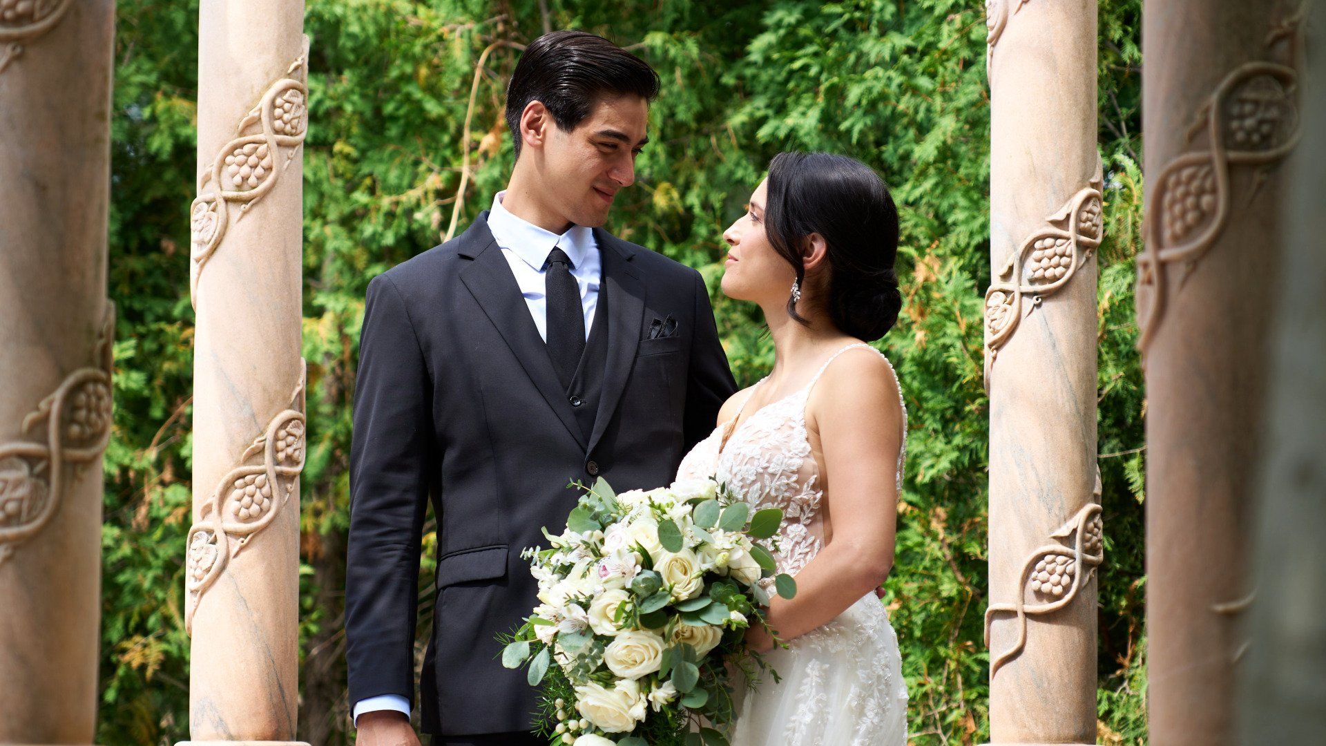 A bride and groom are posing for a picture in front of columns.