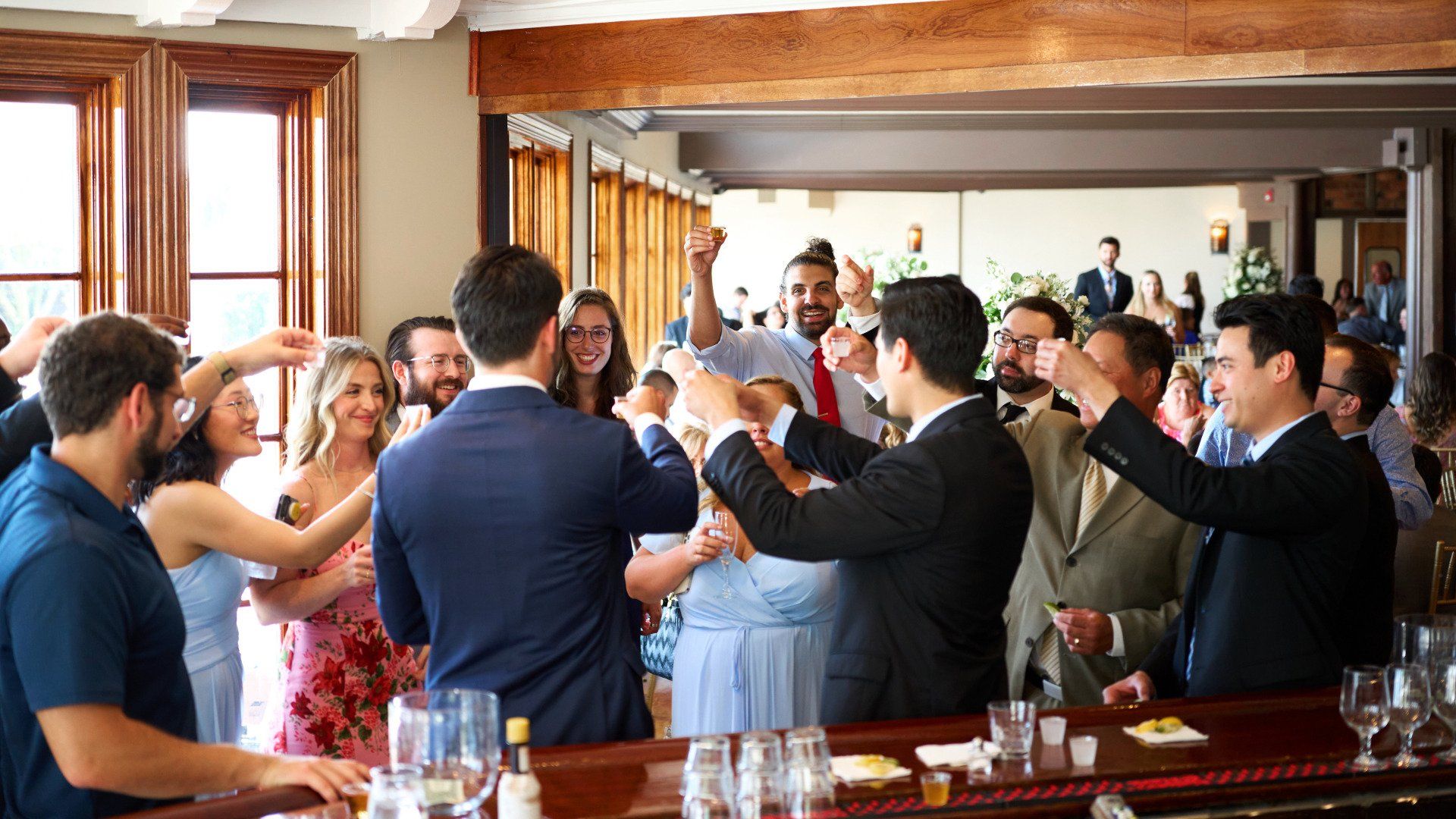 A group of people are standing around a bar toasting each other.