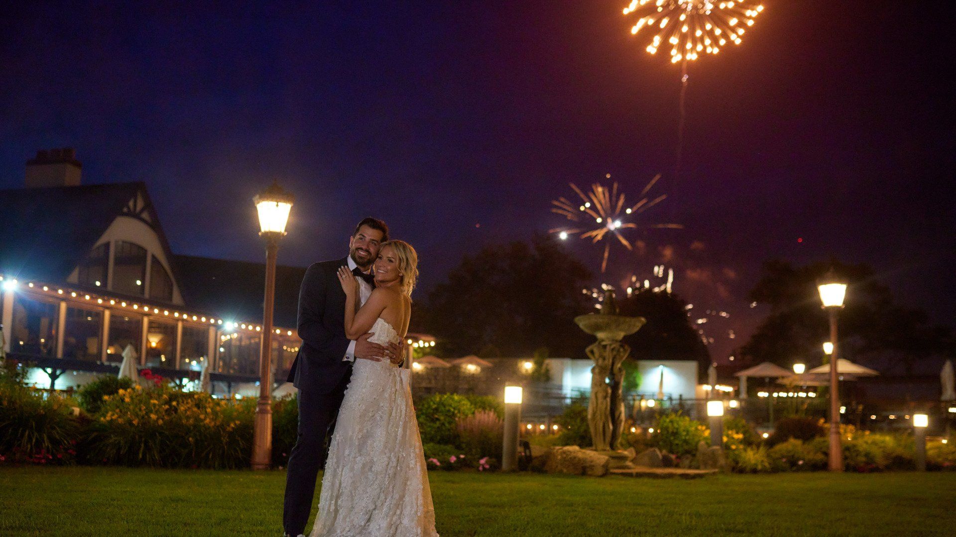 A bride and groom are standing in front of a fireworks display.