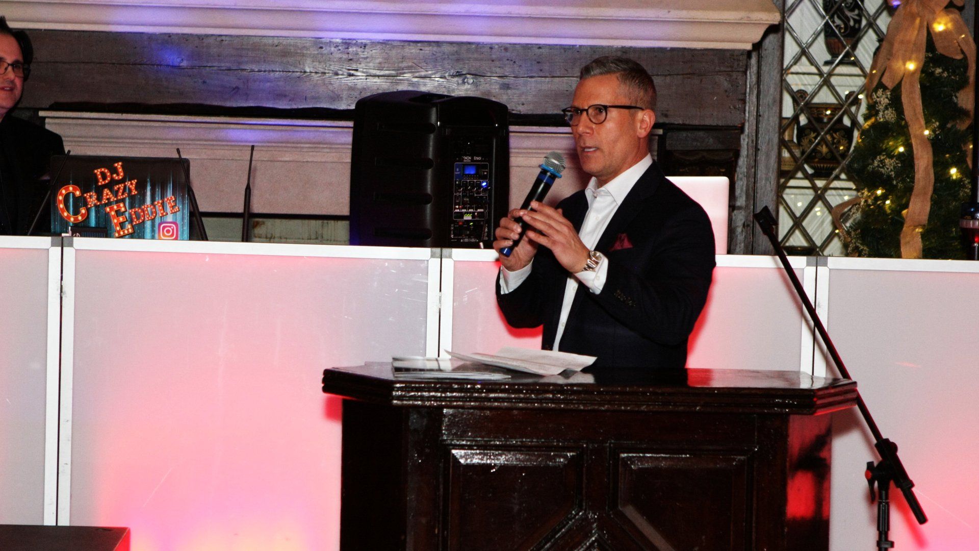 A man in a suit is standing at a podium holding a microphone.
