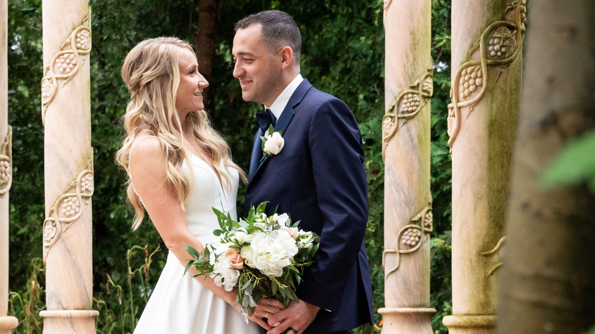 A bride and groom are standing next to each other in front of a gazebo.