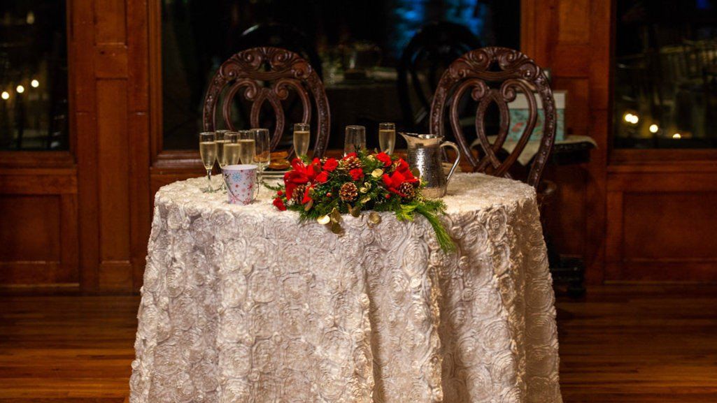 A table with a white tablecloth and red flowers on it.