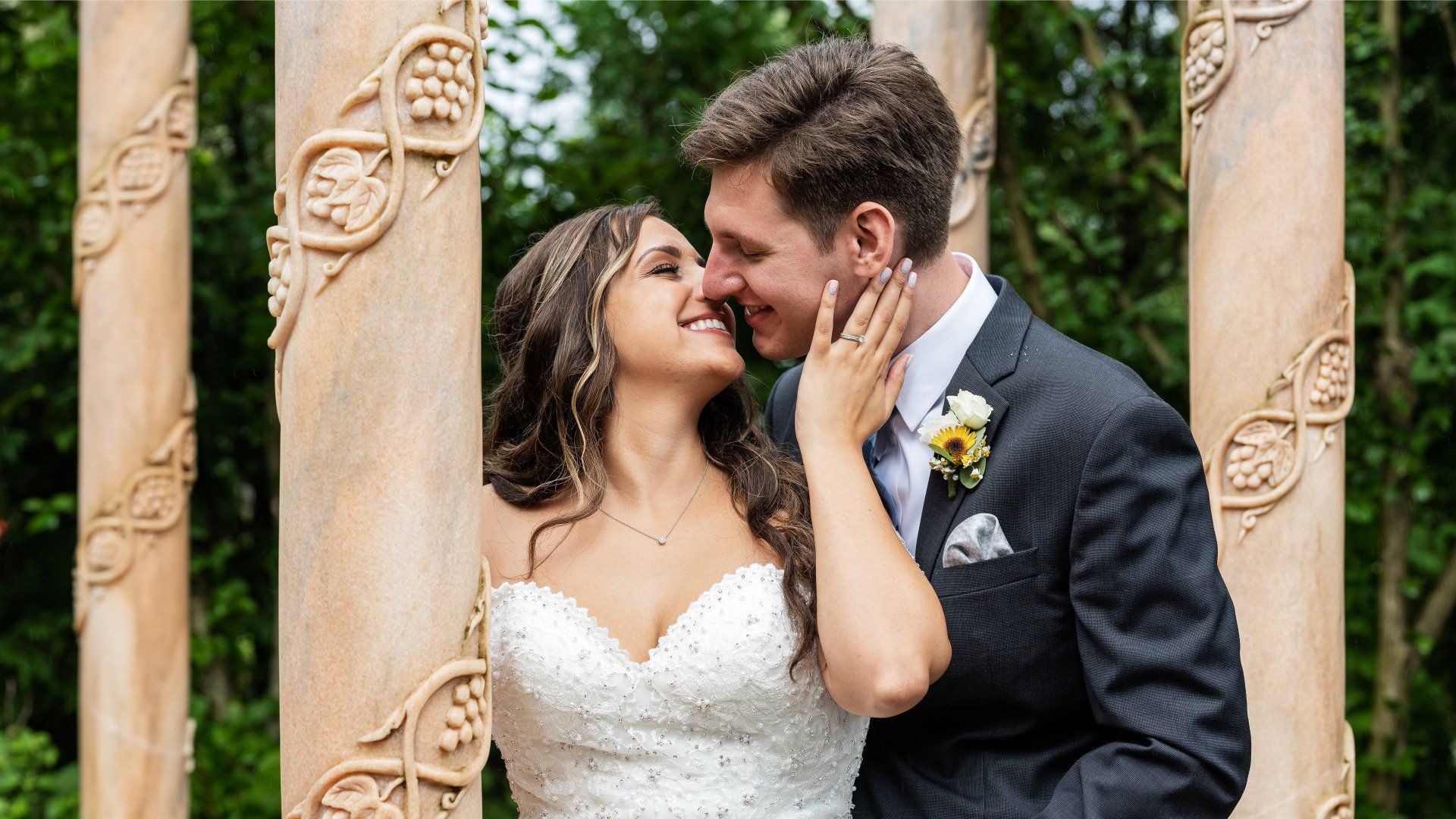 A bride and groom are kissing in front of a row of columns.