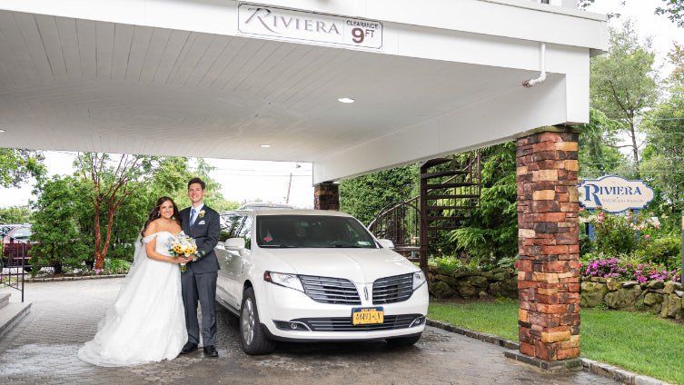 A bride and groom are posing for a picture in front of a white limousine.
