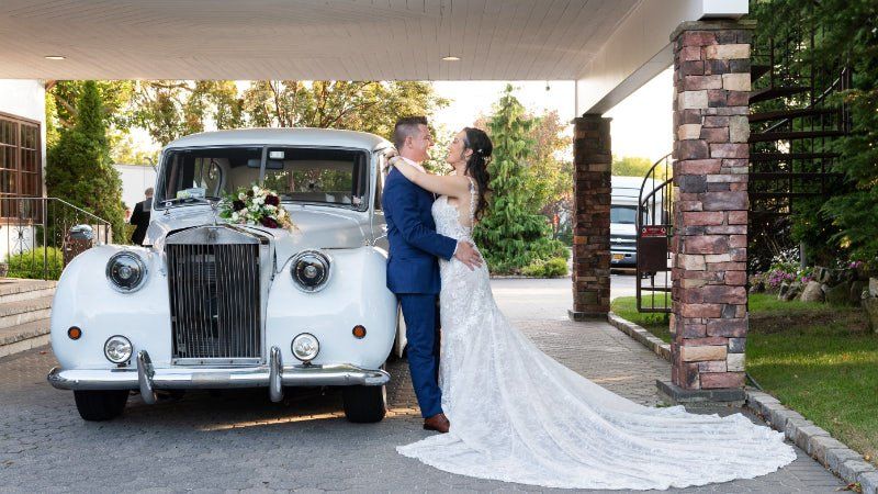 A bride and groom are kissing in front of a white car.