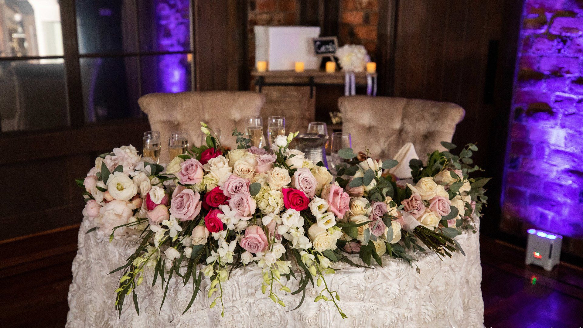 A table with flowers on it and two chairs at a wedding reception.