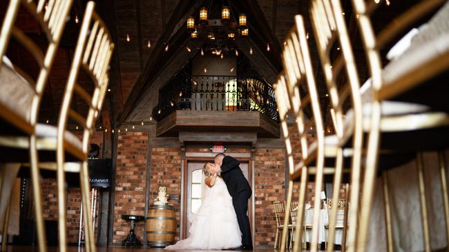 A bride and groom are kissing in a room with gold chairs.