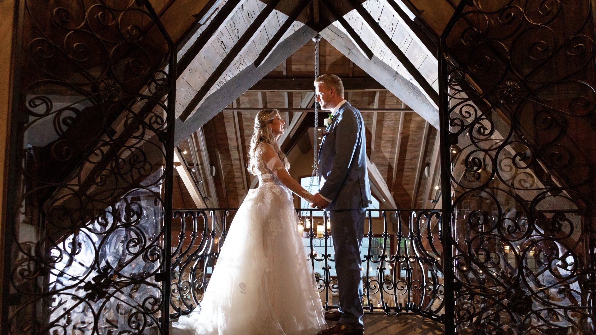 A bride and groom are standing on a balcony holding hands.