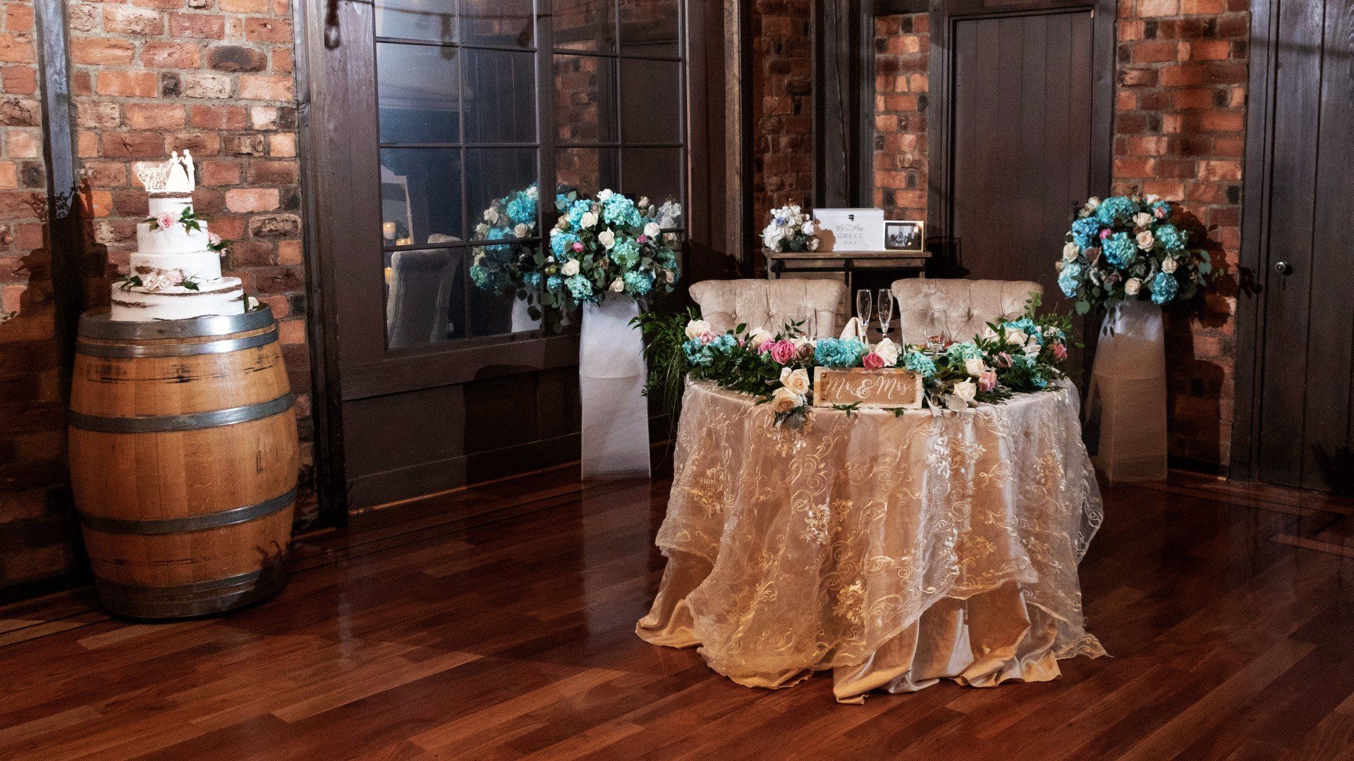 A bride and groom 's table is decorated with flowers and a cake.