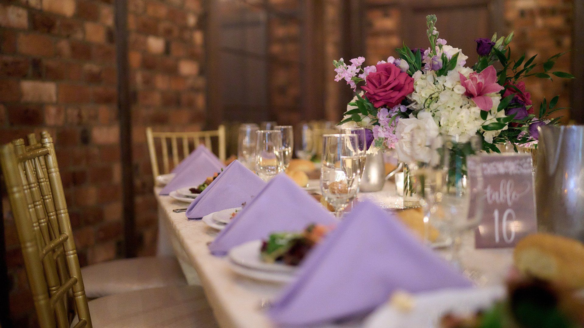 A long table set for a wedding reception with purple napkins and flowers.