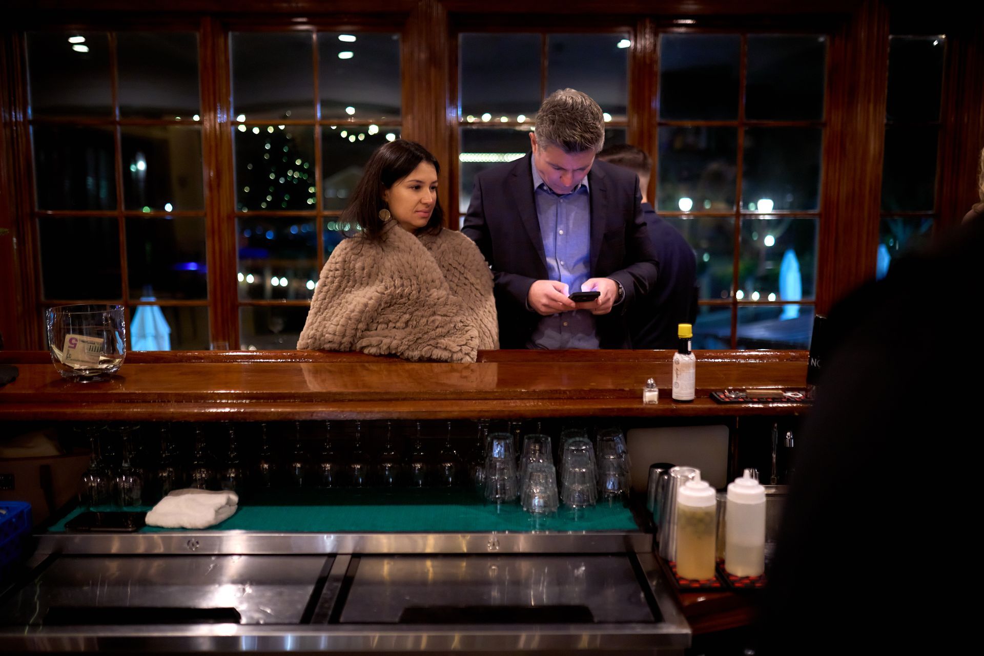 A man and a woman are sitting at a bar looking at their phones.