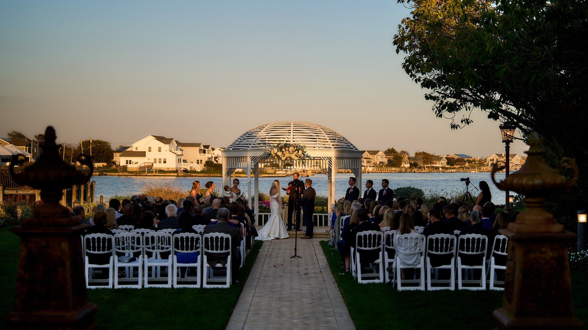 A bride and groom are getting married in front of a gazebo overlooking a body of water.