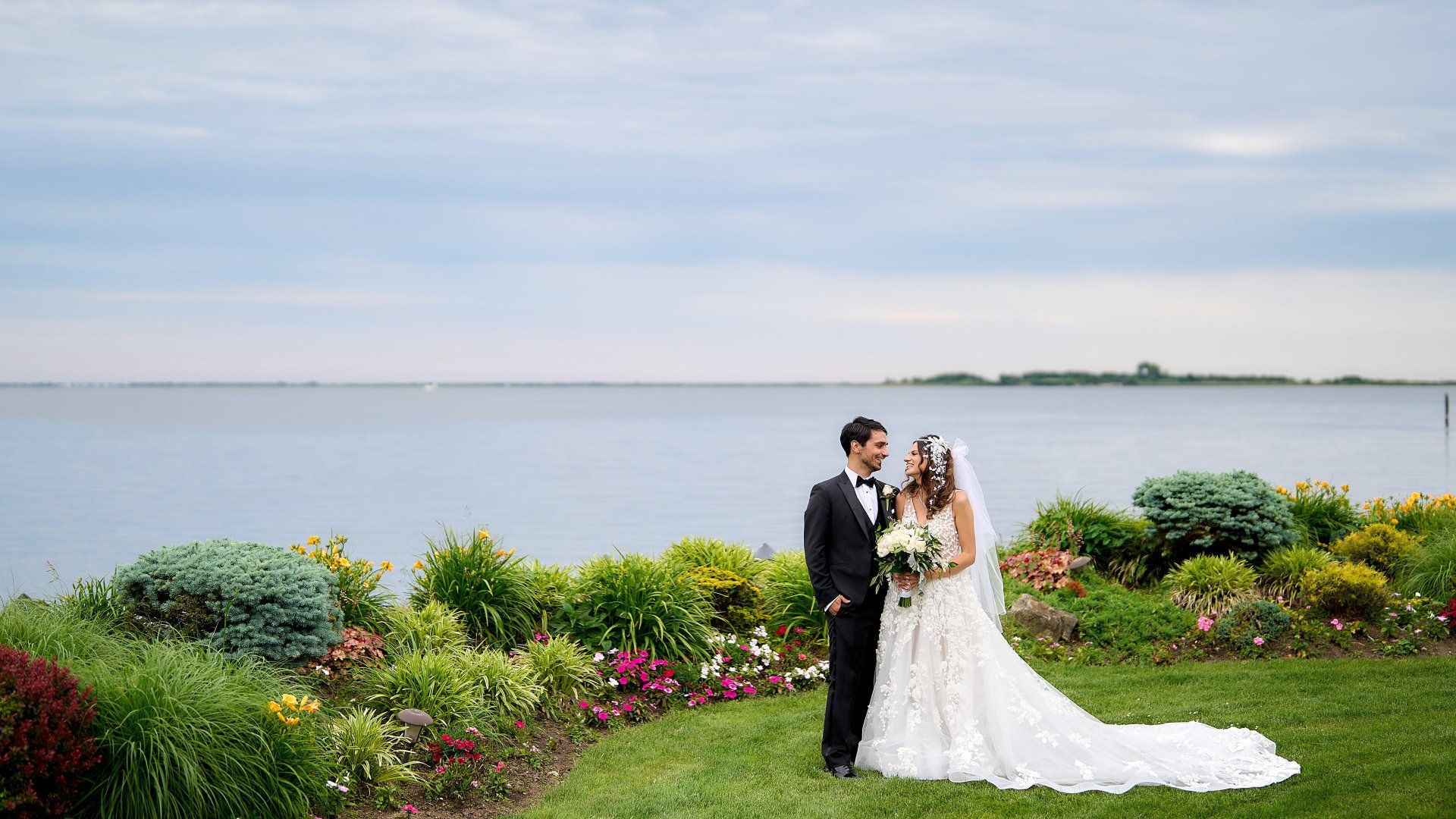 A bride and groom are posing for a picture in front of a body of water.