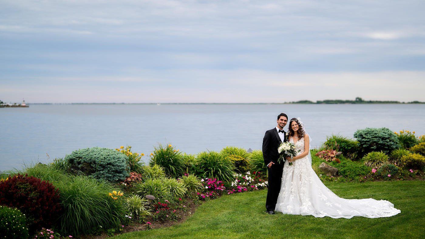 a bride and groom are posing for a picture in front of a body of water .