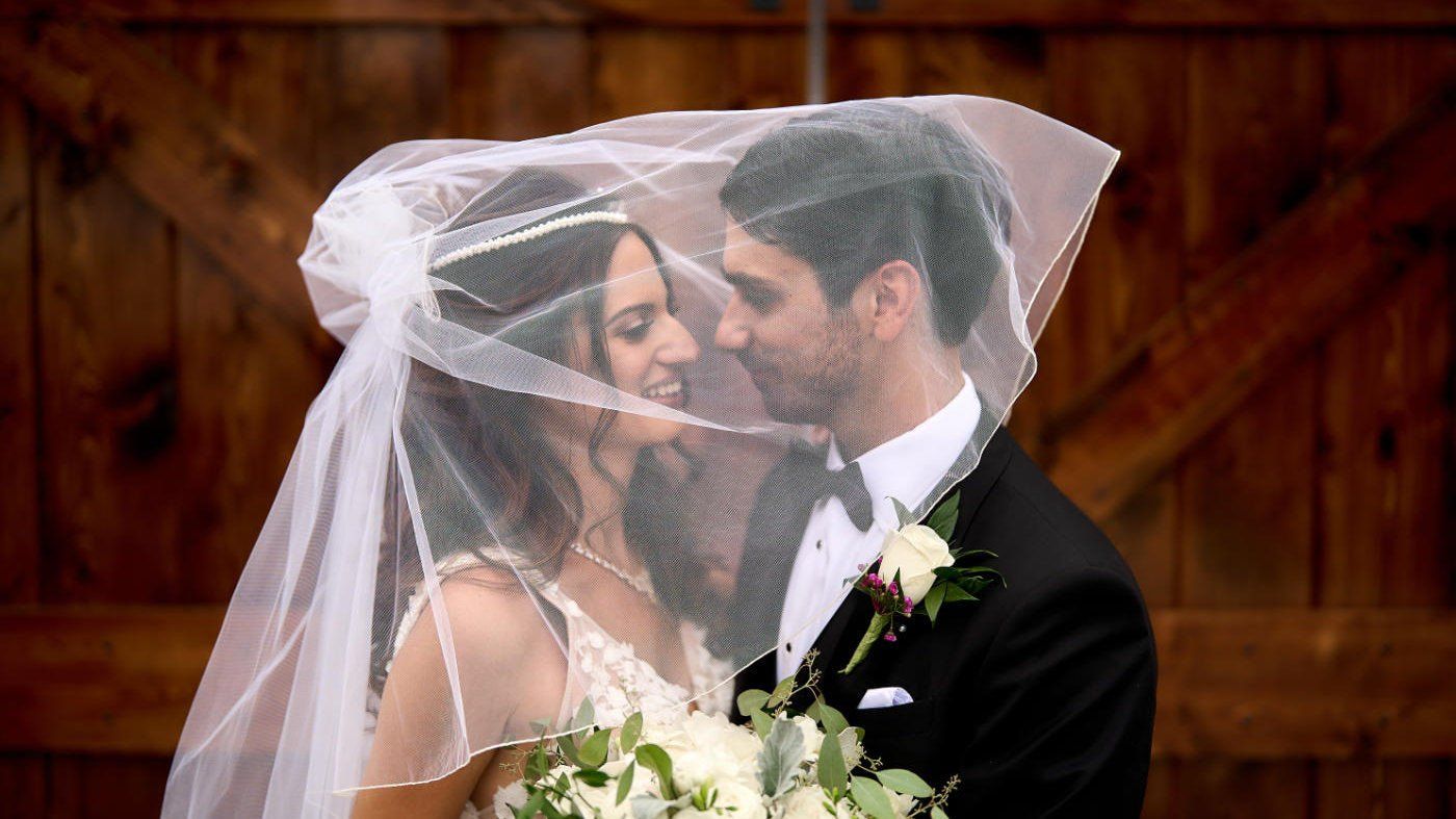 A bride and groom are kissing under a veil.