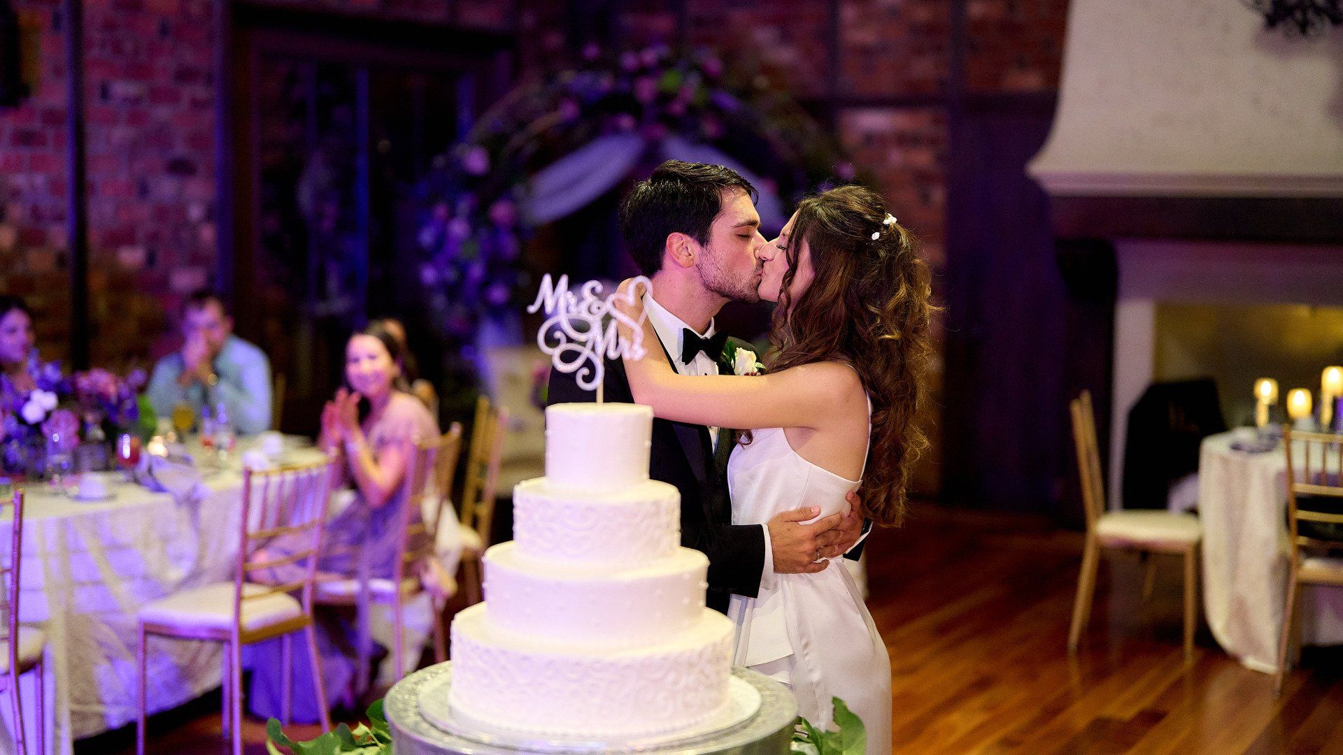 A bride and groom are kissing in front of a wedding cake.