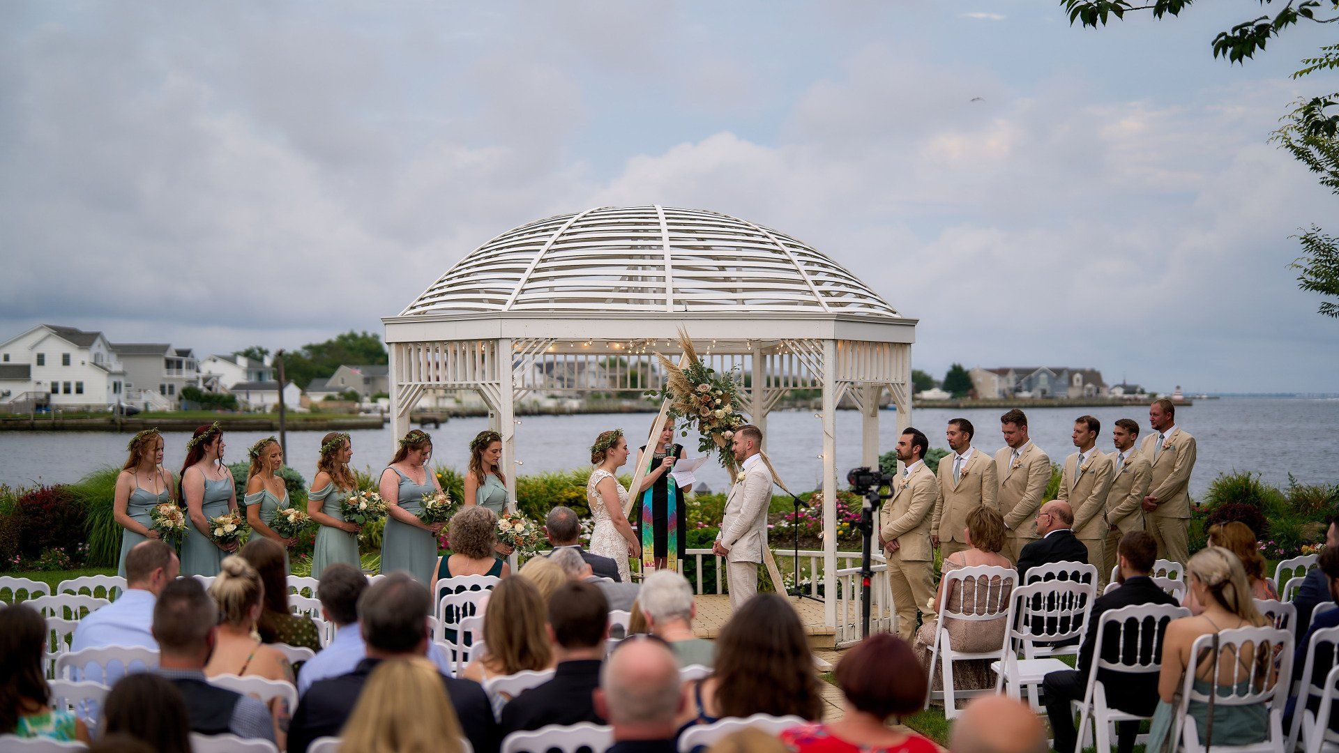 A group of people are sitting in front of a gazebo during a wedding ceremony.