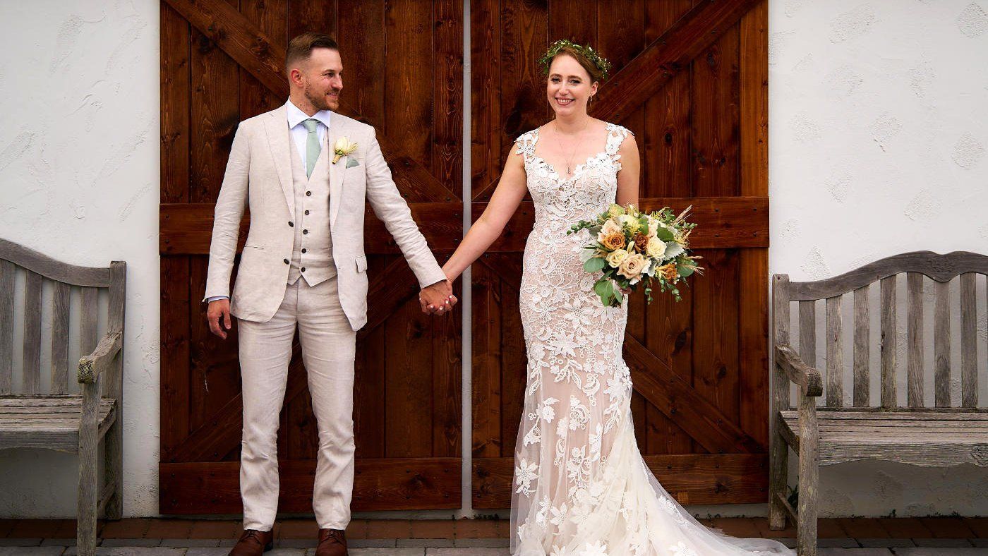 A bride and groom are holding hands in front of a wooden door.