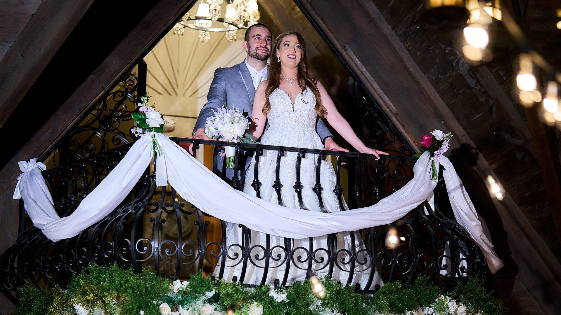 A bride and groom are standing on a balcony decorated with flowers.