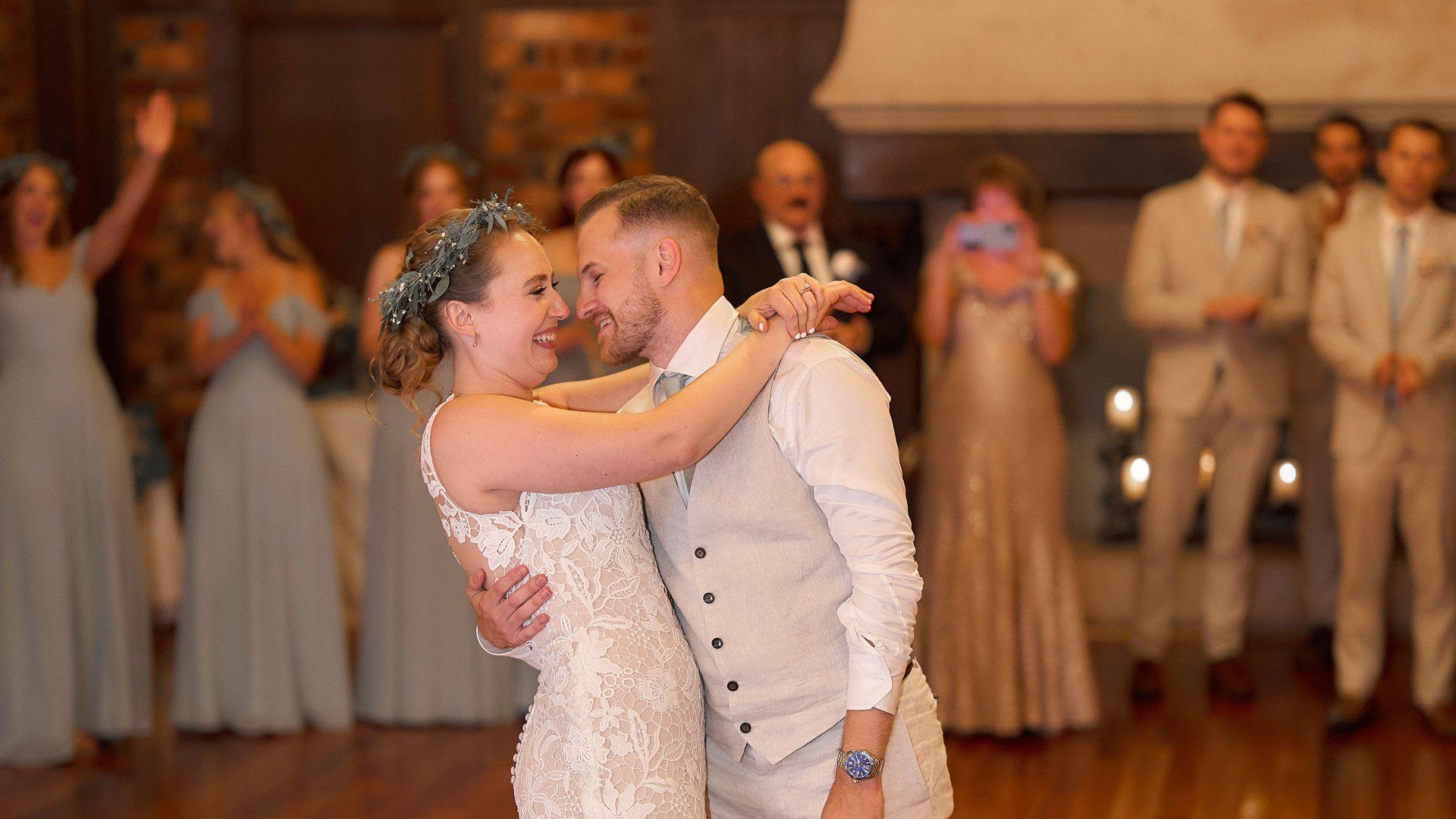 A bride and groom are dancing at their wedding reception in front of their wedding party.