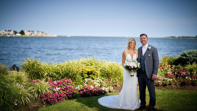 A bride and groom are posing for a picture in front of a body of water.