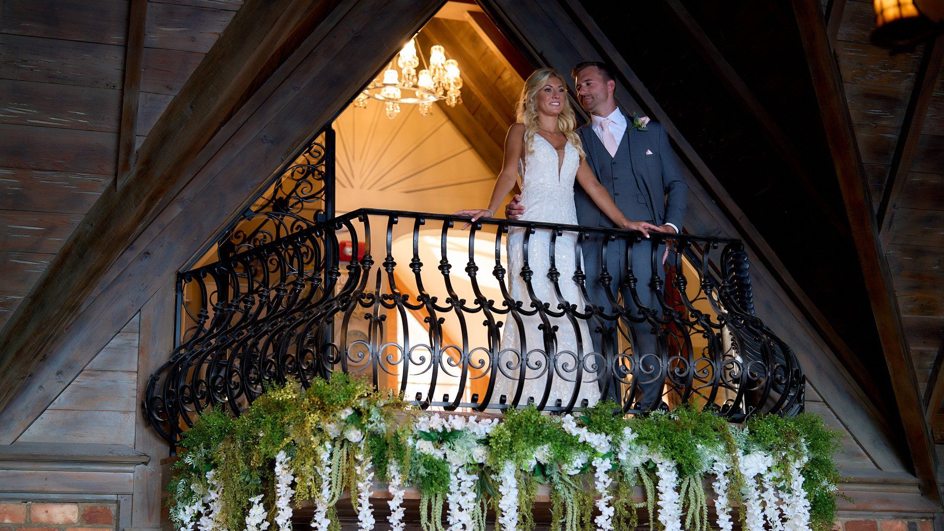 A bride and groom are standing on a balcony holding hands.