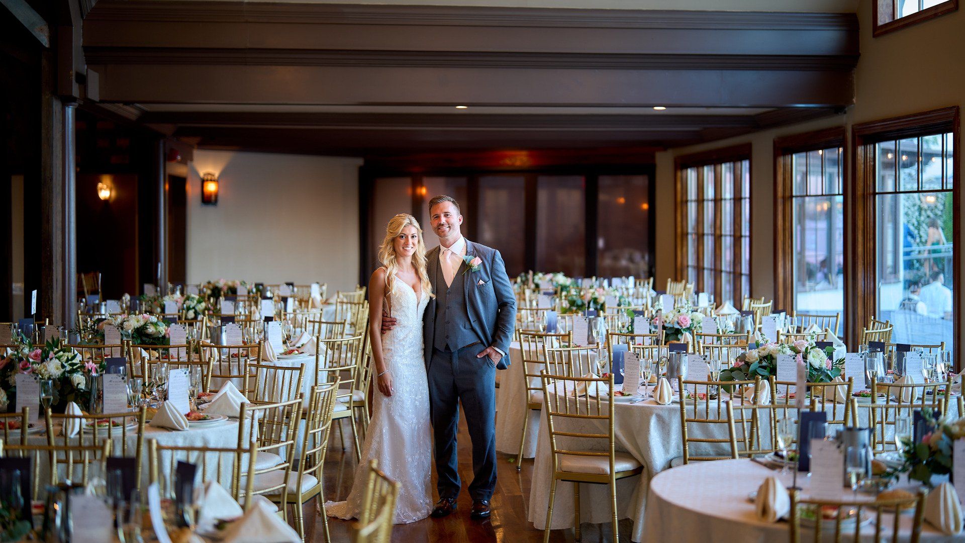 A bride and groom are posing for a picture in a large room filled with tables and chairs.