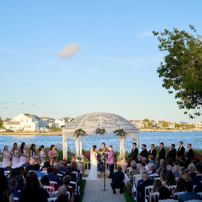 A bride and groom are getting married under a gazebo overlooking a body of water