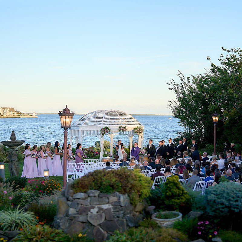 A wedding ceremony is taking place in front of a gazebo overlooking the ocean