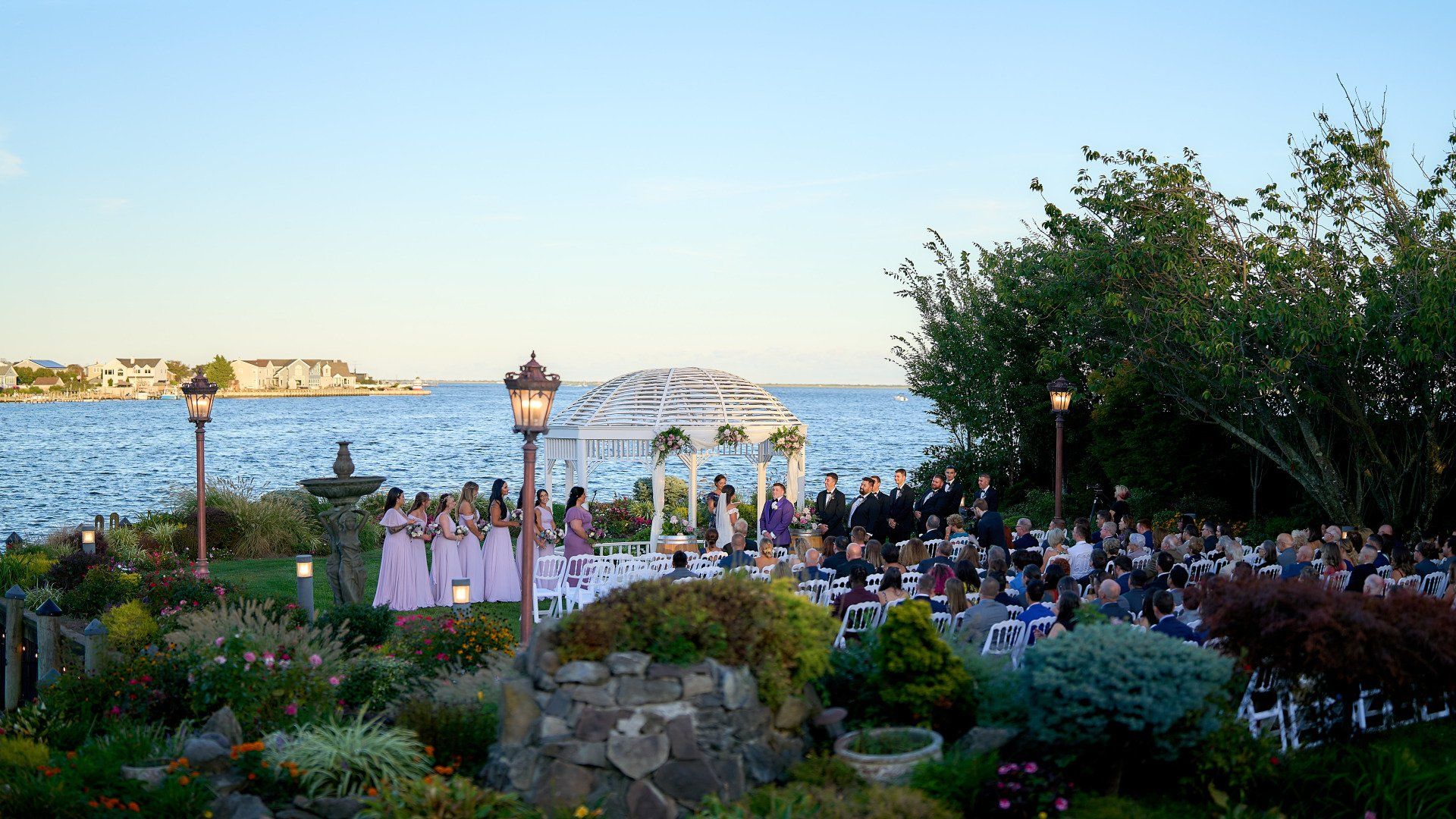A wedding ceremony is taking place in front of a gazebo overlooking the ocean.