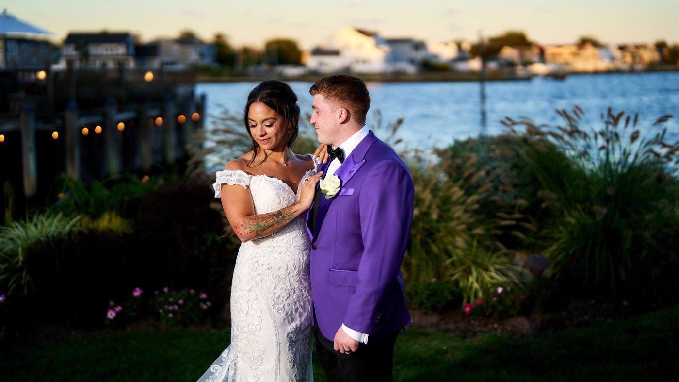 A bride and groom are standing next to each other in front of a body of water.