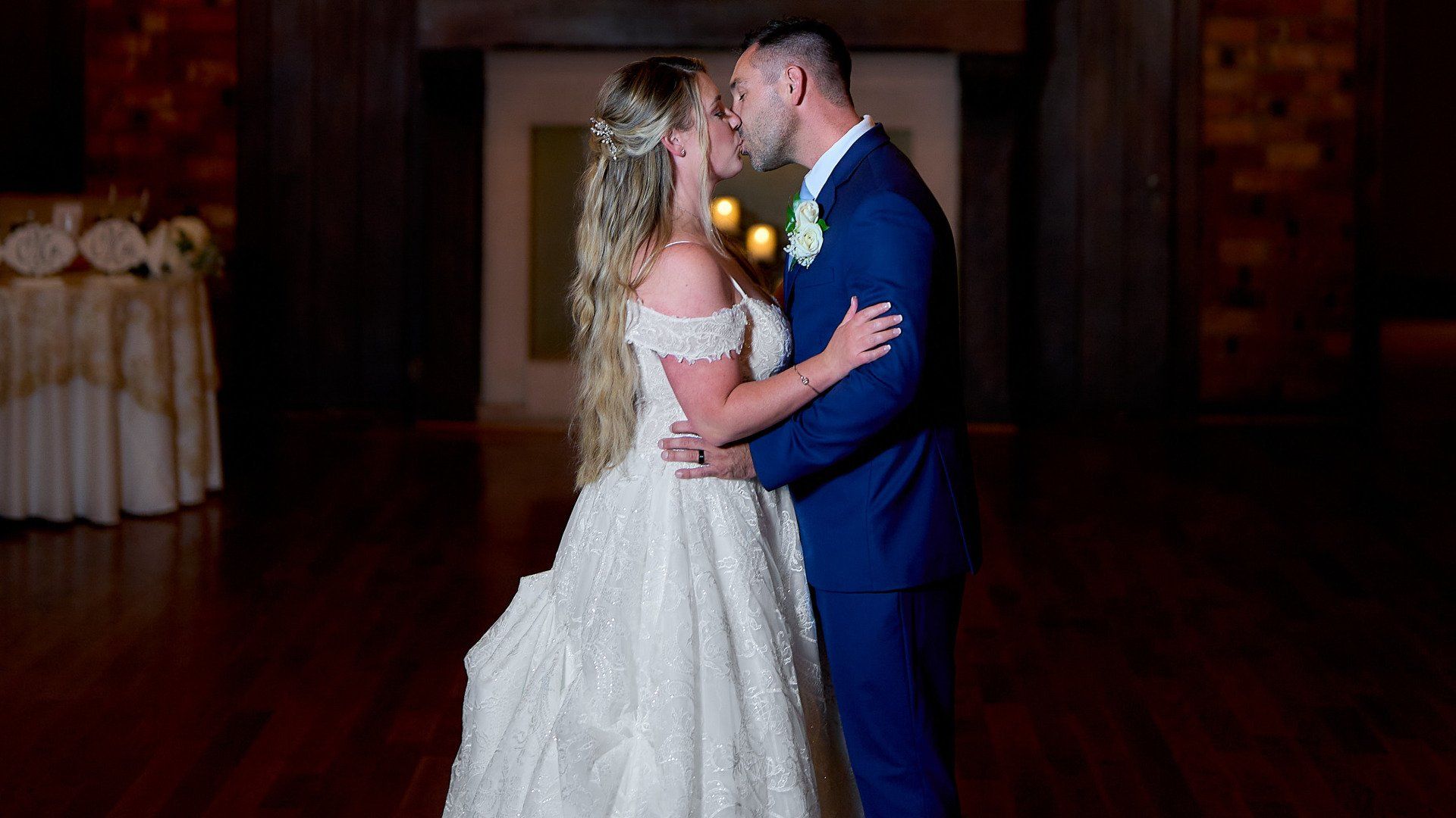 A bride and groom are kissing in a dark room at their wedding reception.