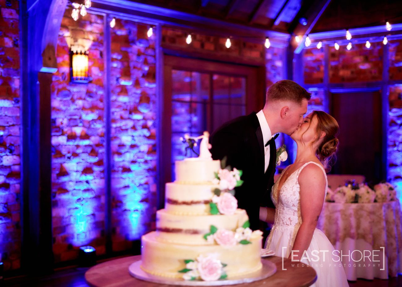 A bride and groom are kissing in front of a wedding cake.