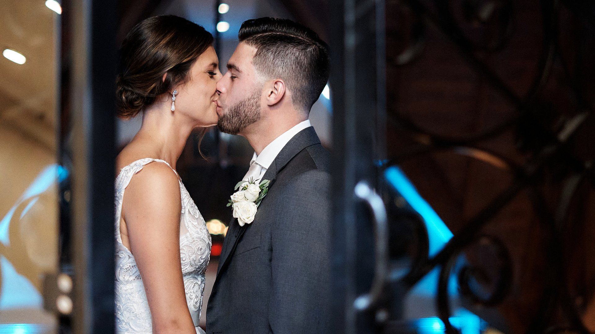 A bride and groom are kissing in front of a window.