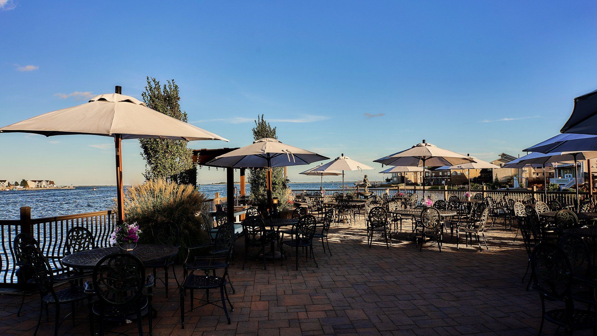 A patio with tables and chairs and umbrellas overlooking the water.