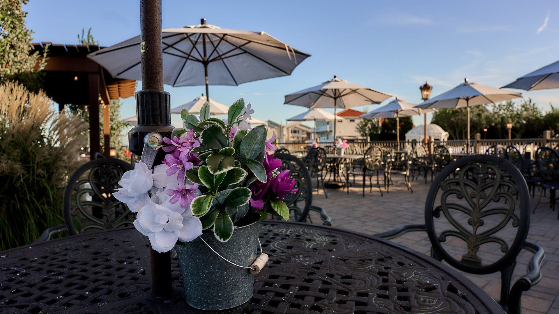 A bucket of flowers is sitting on a table under an umbrella.