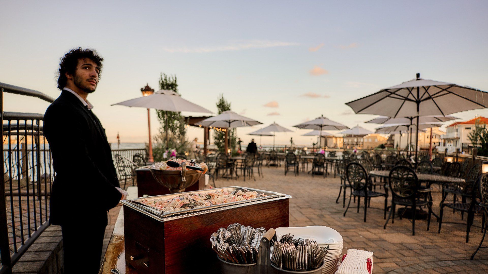 A man in a suit stands in front of a buffet table with umbrellas.