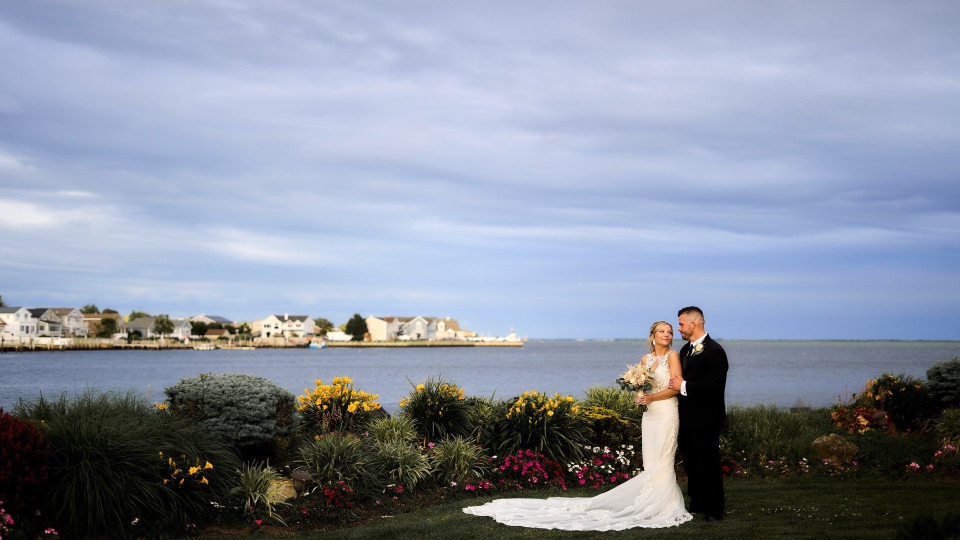 A bride and groom are posing for a picture in front of a body of water.