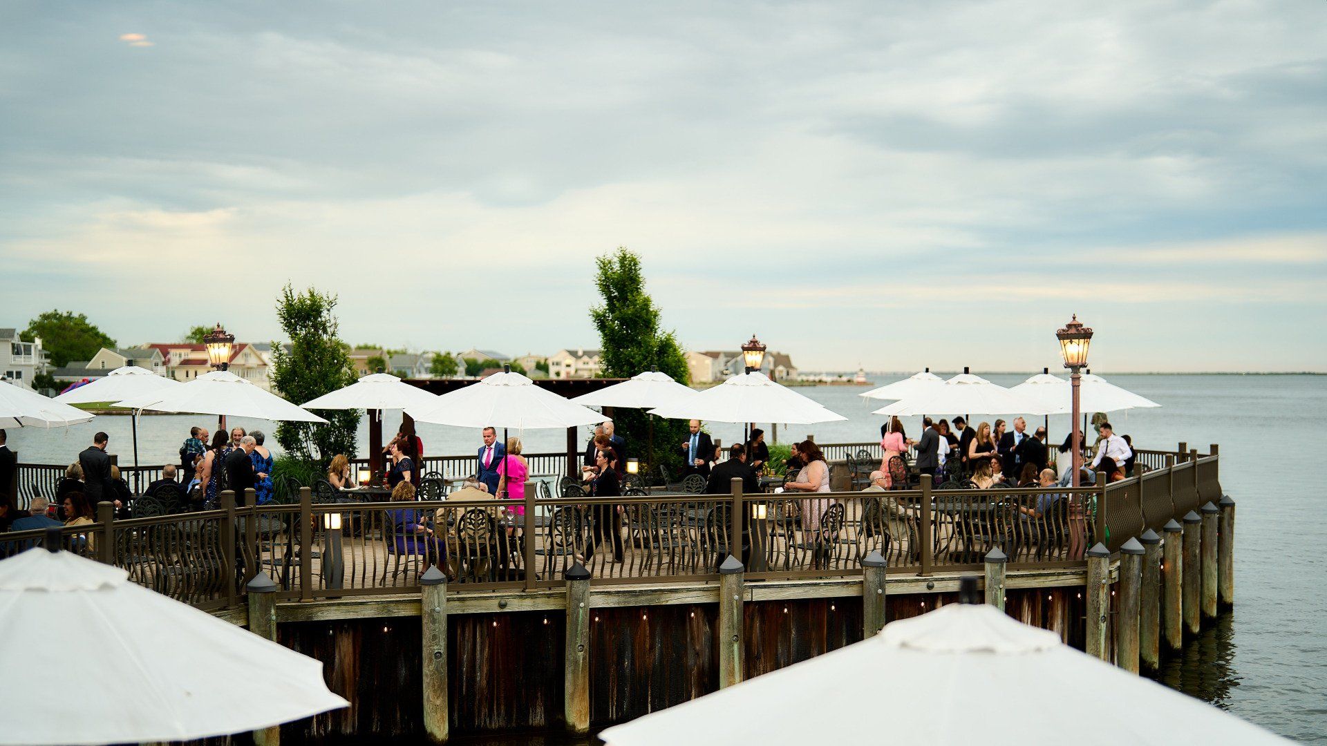 A group of people are sitting under umbrellas on a pier overlooking the water.