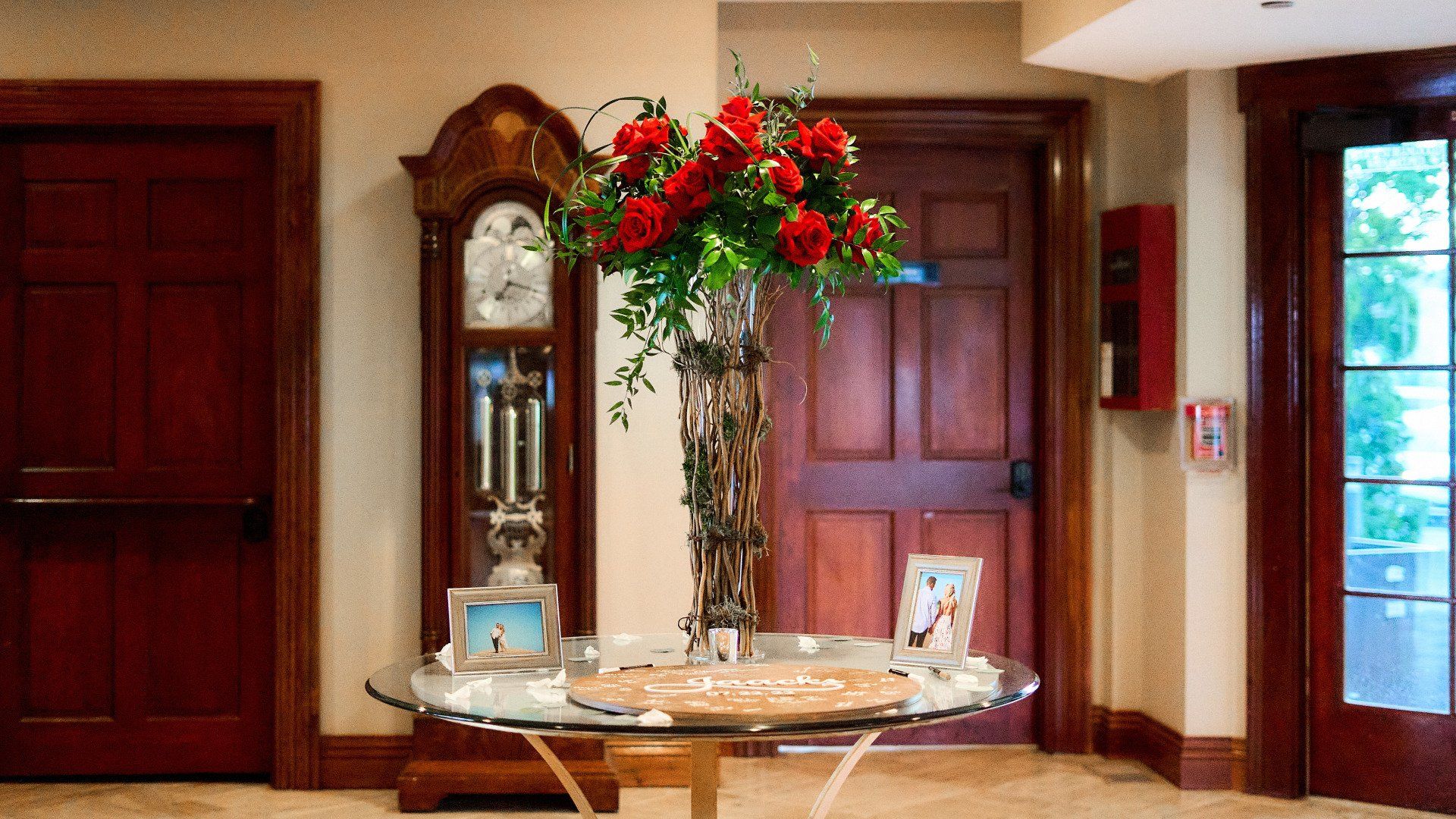 A vase of flowers is sitting on a table in front of a grandfather clock.