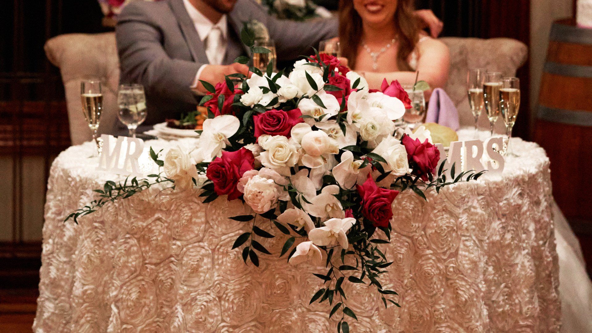 A bride and groom are sitting at a table with flowers and champagne glasses.