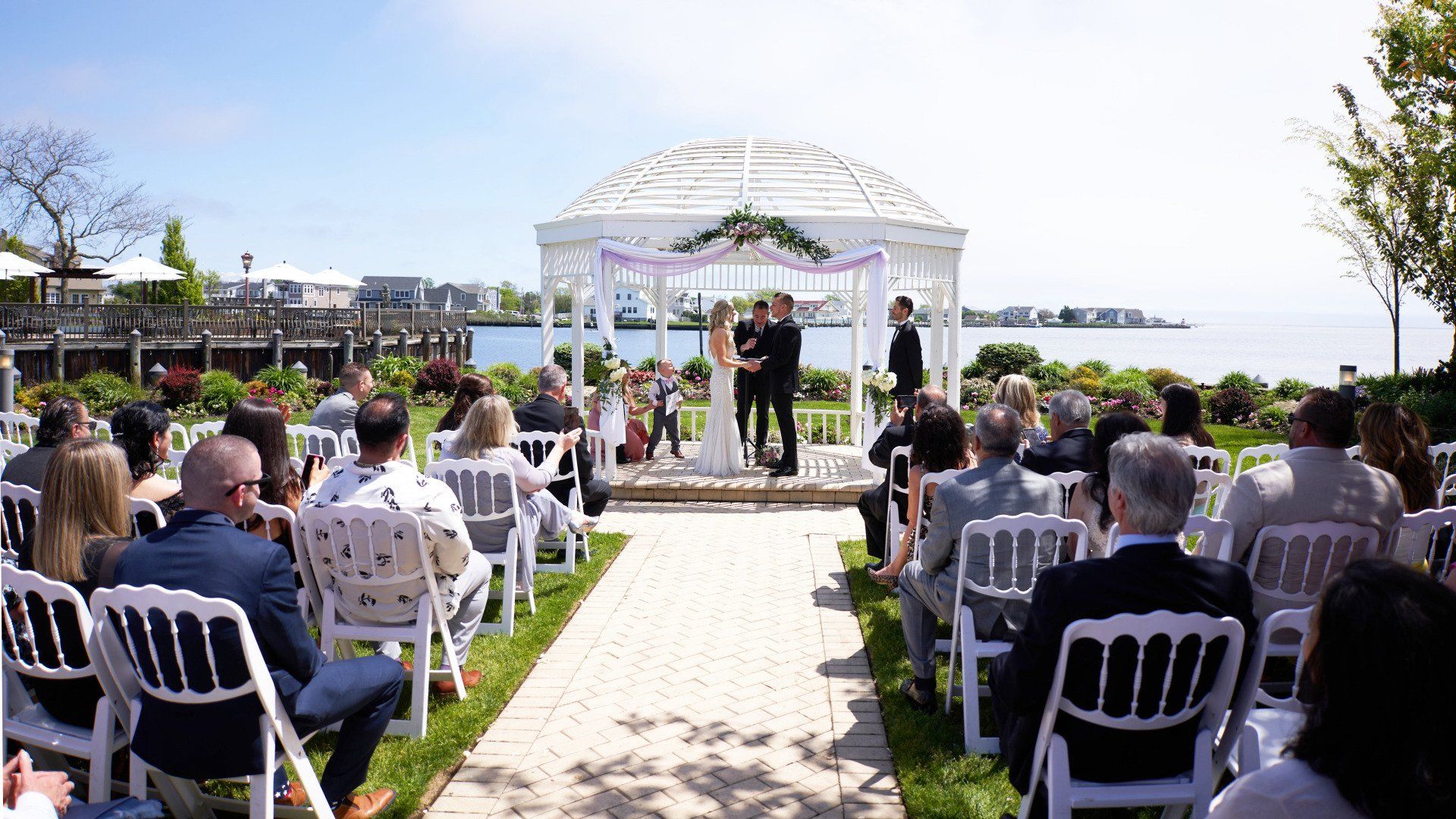 A group of people are sitting in chairs at a wedding ceremony under a gazebo.