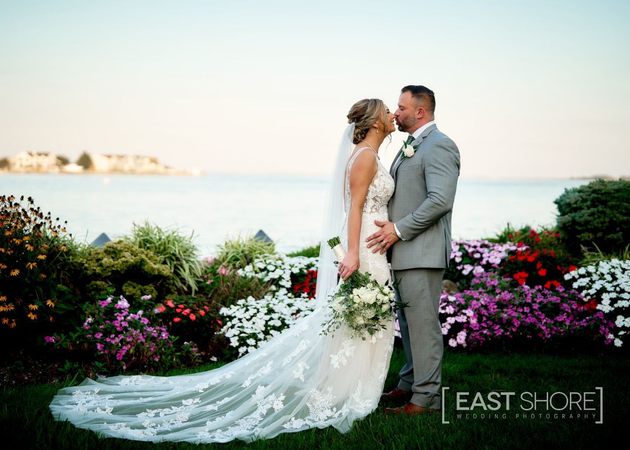 A bride and groom are kissing in front of a flower garden.