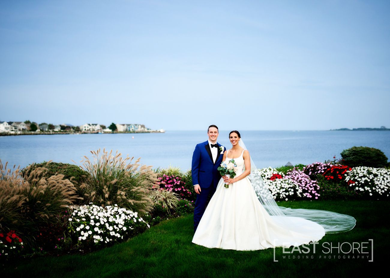 A bride and groom pose for a picture in front of a body of water