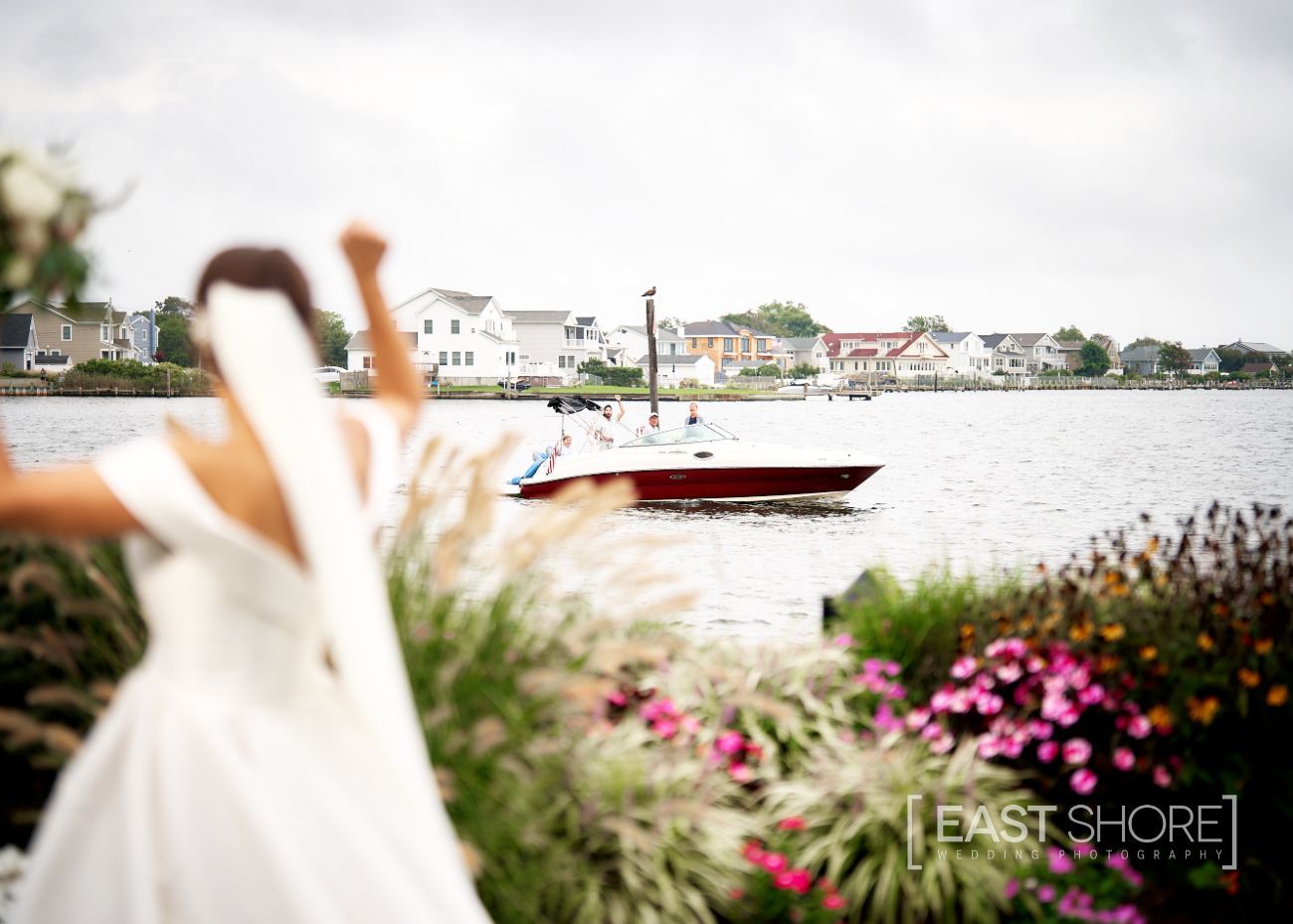 A bride in a white dress stands in front of a body of water